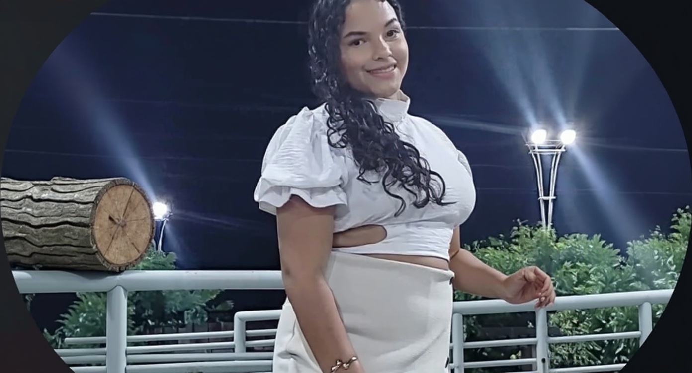 A woman is standing outside in a white outfit. The background includes trees and lights.